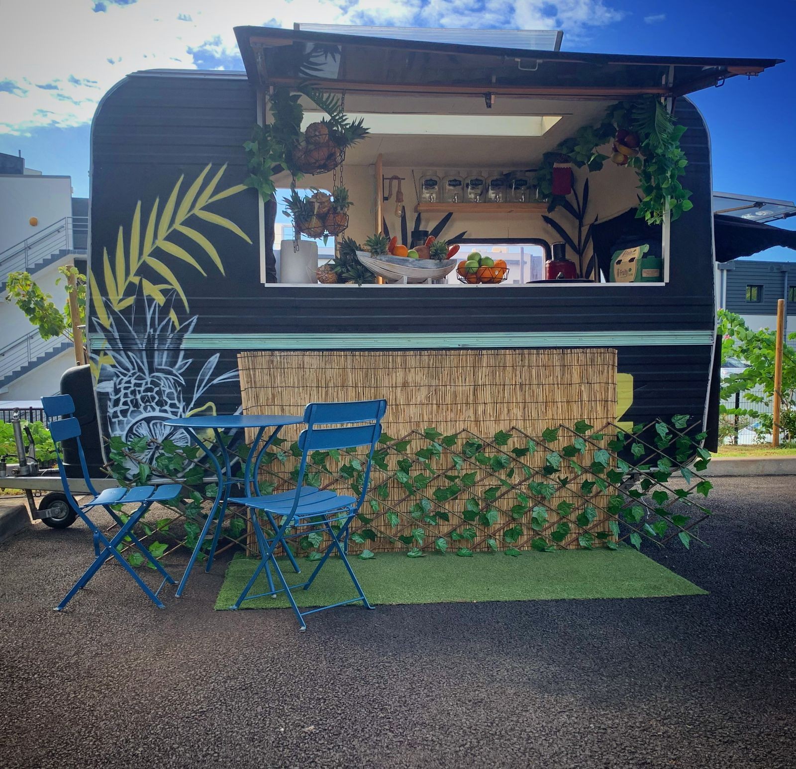 Colorful food truck with tropical decor and outdoor seating on a sunny day.